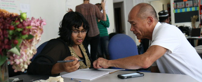 woman writing on table supported by a man